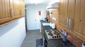 A narrow kitchen with wooden cabinets, a stove, and a tiled backsplash. - A&A Apartment Basildon with free parking  (Basildon)