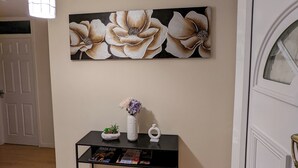 A hallway with a black console table, a floral painting, a white door, and a hanging light fixture. - A&A Apartment Basildon with free parking  (Basildon)