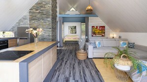 Ein modernes Loft mit Küche, Essbereich und Wohnzimmer. Es verfügt über eine Steinwand, Holzboden und eine geneigte Decke.