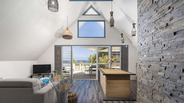 Ein modernes Wohnzimmer mit einer Couch, einem Fernseher und einem Essbereich mit Tisch und Stühlen. Ein großes Fenster bietet einen Blick ins Freie.