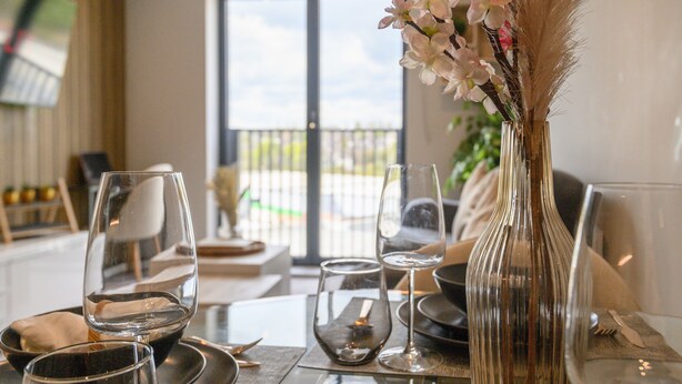 Una mesa de comedor dispuesta con copas de vino, platos y un jarrón con flores.