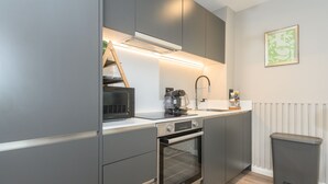 Una cocina moderna con armarios grises, un horno empotrado, una cafetera y una escalera apoyada en la pared.