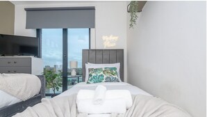 Una habitación de hotel moderna con una cama, un televisor, una mesita de noche con una lámpara y un letrero de neón que dice 