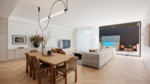 Un espacio moderno con comedor, sofá, televisor y zona de piscina.