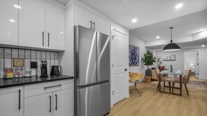 A modern kitchen with white cabinets, a stainless steel refrigerator, and a dining area with a table and chairs. - Luxury : Cozy| Modern| Clean| Spacious| easy Access to major routes in Calgary (Calgary)