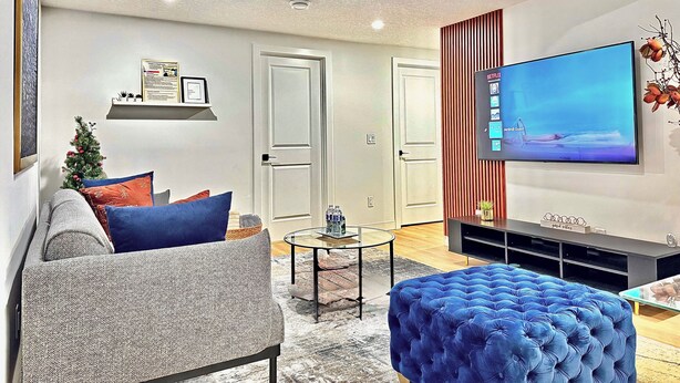 A modern living room with a grey sofa, blue ottoman, and a flat-screen TV on the wall. - Luxury : Cozy| Modern| Clean| Spacious| easy Access to major routes in Calgary (Calgary)