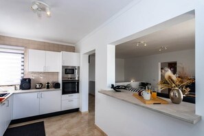 Una cocina moderna con gabinetes blancos, electrodomésticos de acero inoxidable y una barra de desayuno con un florero de flores secas.