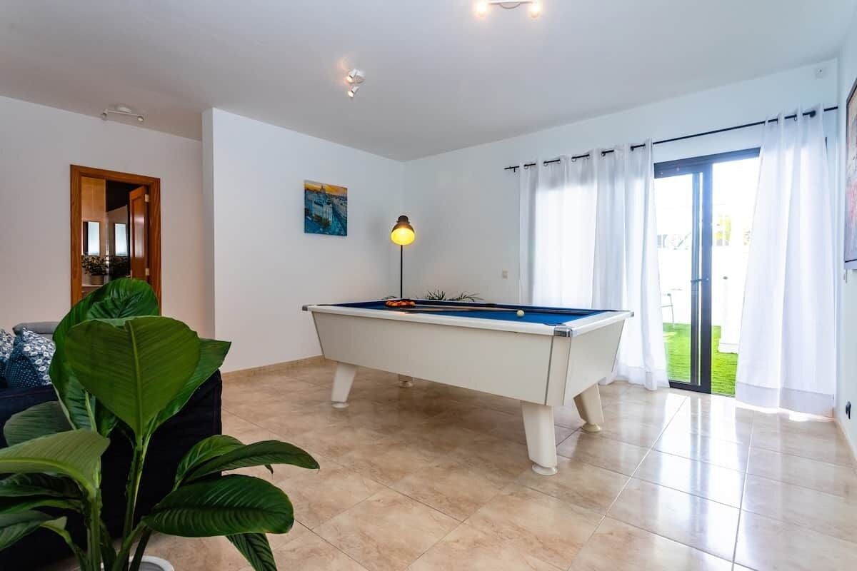 A room with a pool table, a lamp, a door, and a view of the outdoors.