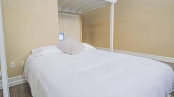 A bedroom with a bunk bed, white bedding, a bedside lamp, and a door in the background.