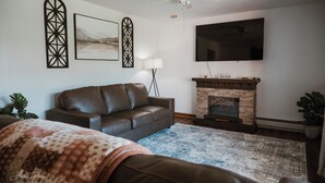 A living room with a leather sofa, a fireplace, a flat-screen TV, and decorative wall art.