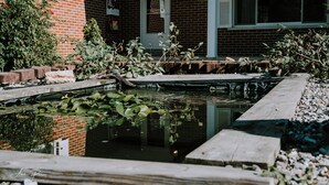 A brick building with a pond, wooden deck, and greenery.