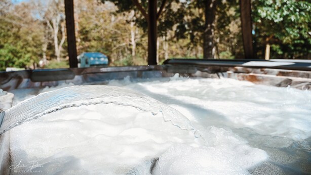 A hot tub with a wooden structure and a view of trees and a blue car in the background.
