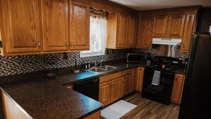 A kitchen with wooden cabinets, a granite countertop, a stainless steel range hood, a black refrigerator, and a tiled backsplash.