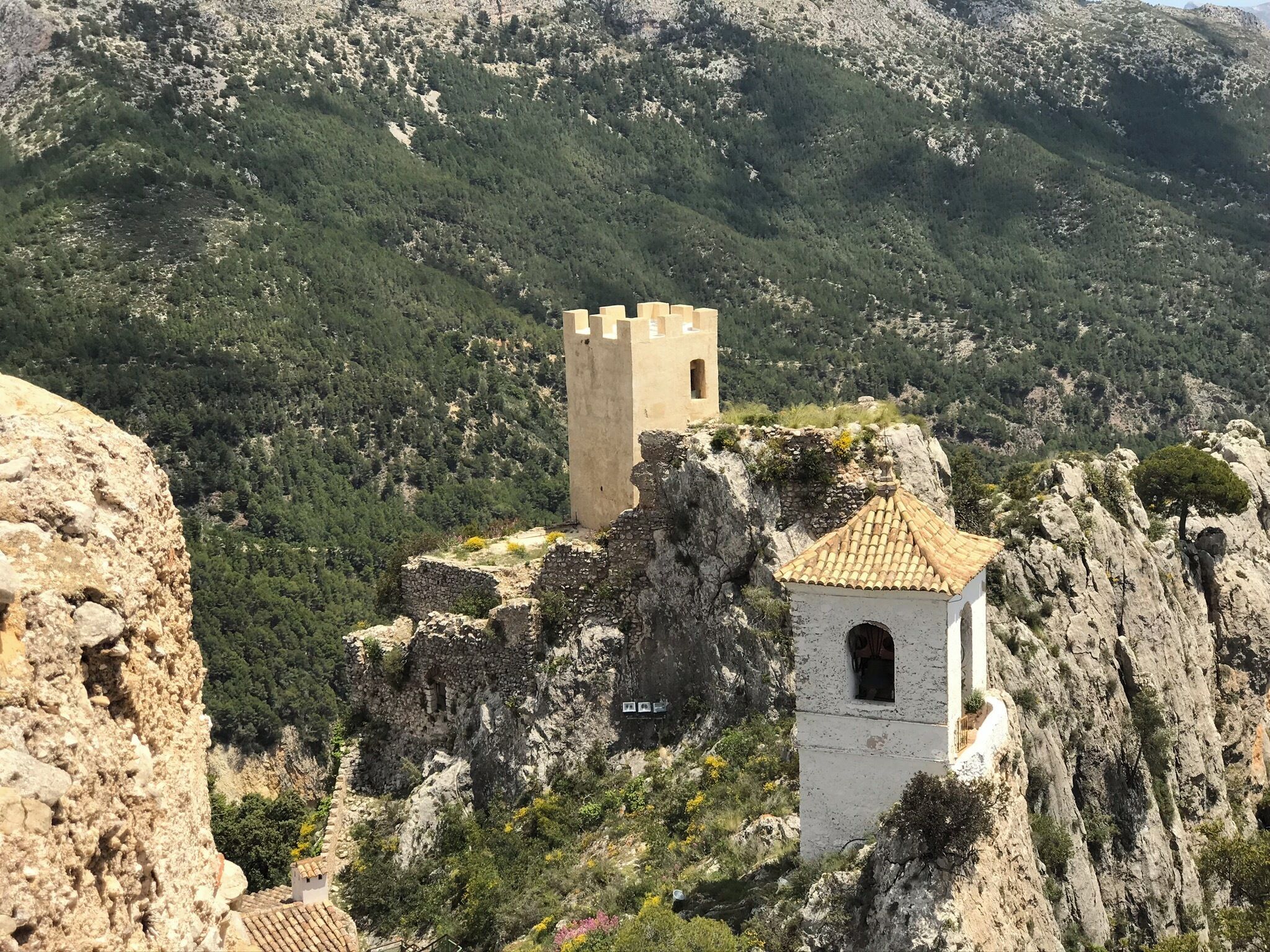 A stone tower and a small building with a tiled roof on a rocky hillside.