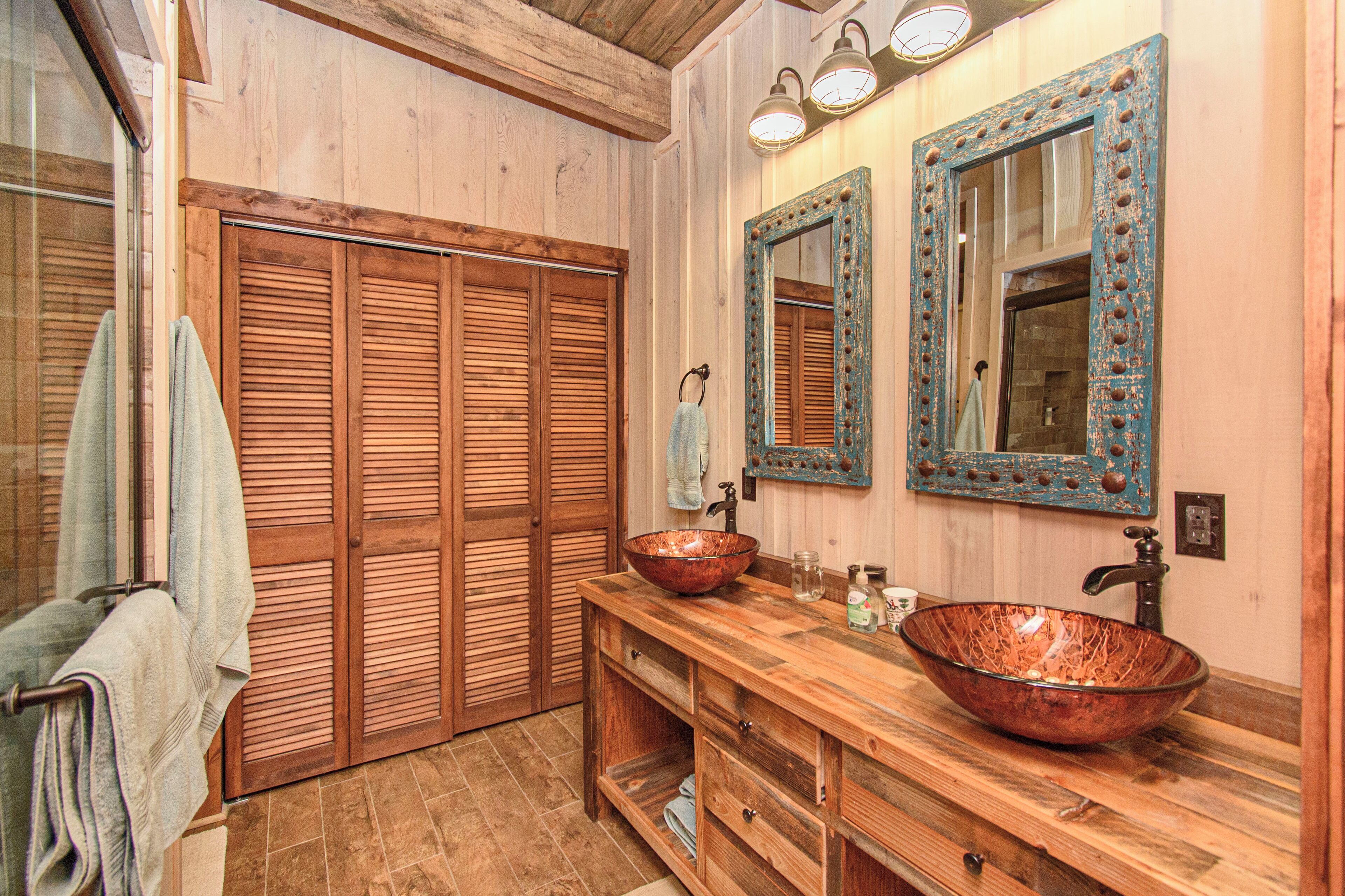 A bathroom with wooden cabinets, a large copper sink, and a mirror with decorative frame.