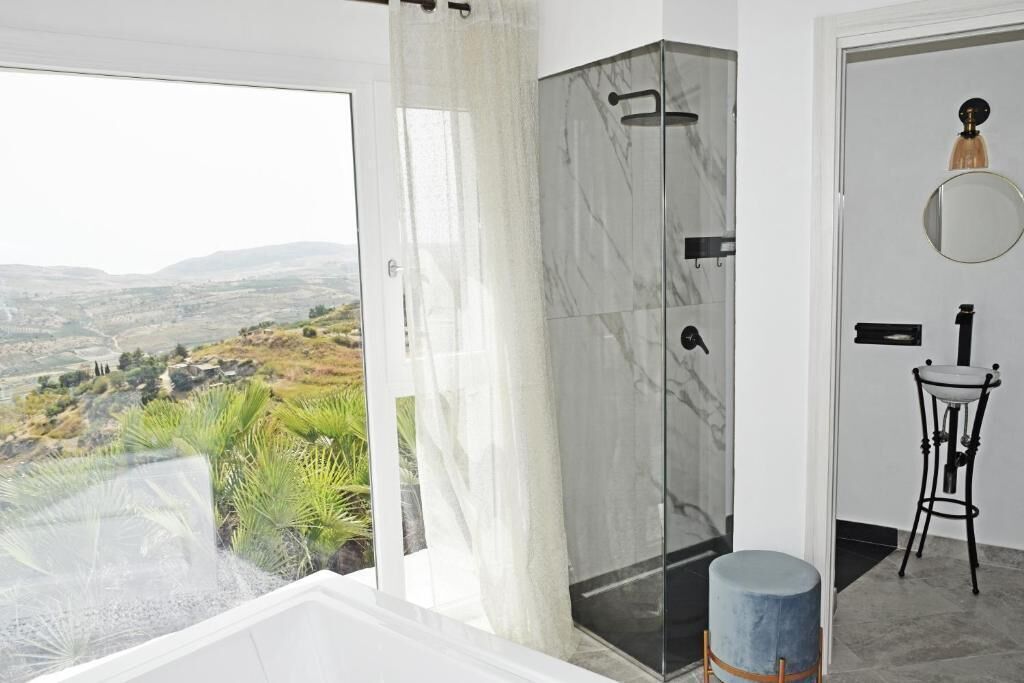 A modern bathroom with a glass shower enclosure, a bathtub, and a view of a valley.