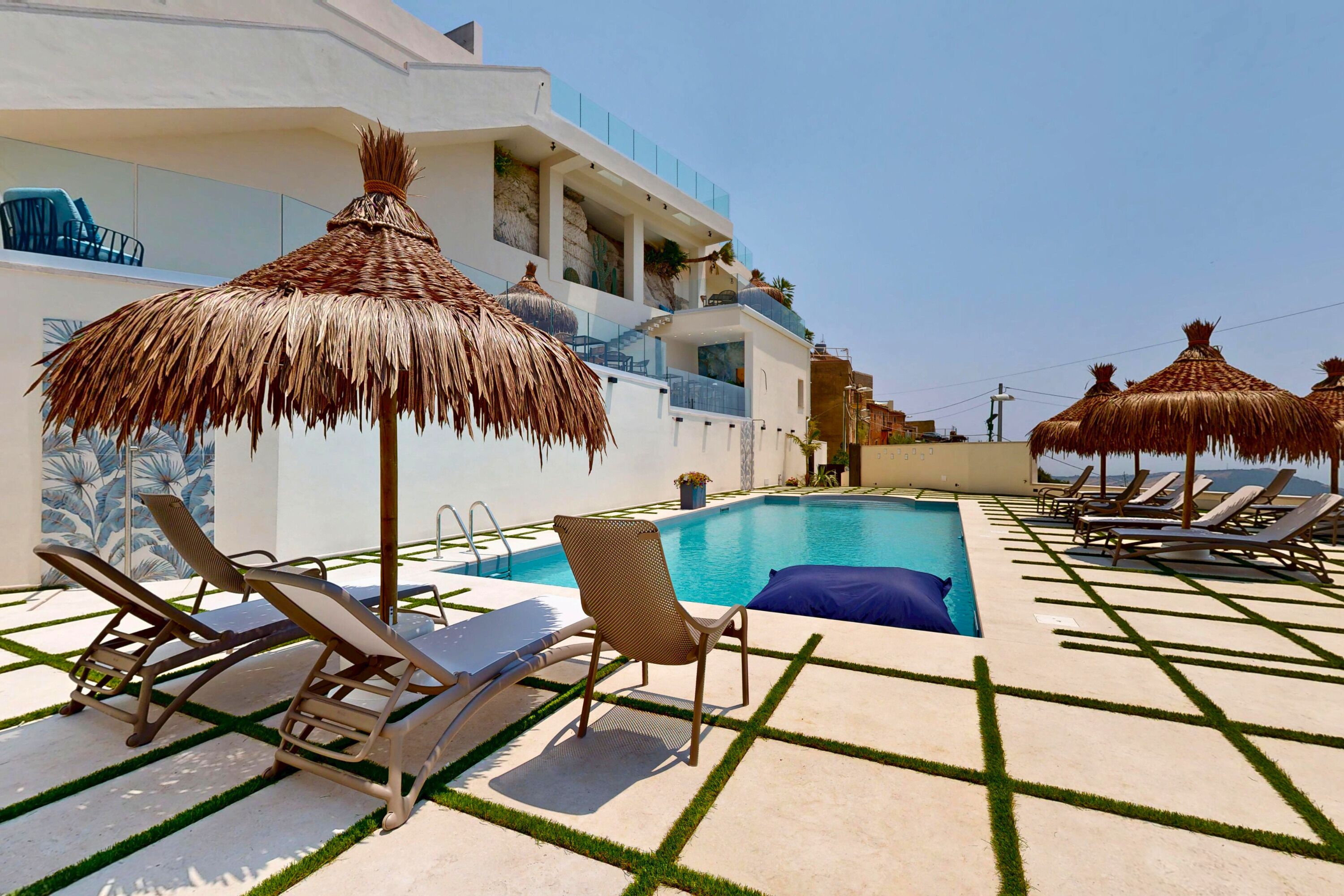 A poolside area with lounge chairs, a thatched umbrella, and a clear blue sky.