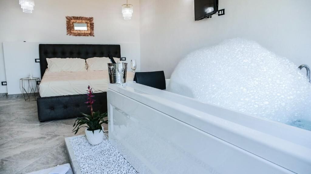 Ett modernt sovrum med en stor säng, ett badkar fyllt med bubblor, en krukväxt och ett litet bord.