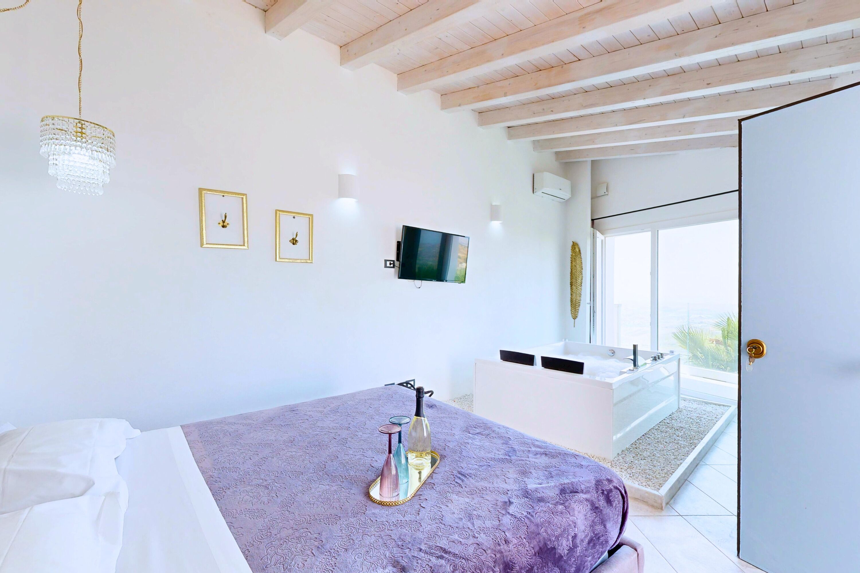 A bedroom with a bed, a television, a bathroom with a bathtub, and a balcony.