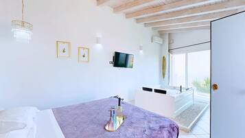 A bedroom with a bed, a television, a bathroom with a bathtub, and a balcony.