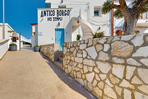 A building with a sign reading 'ANTICO BORGO DEI TEMPLI,' a stone wall, and a tree. - Antico borgo dei templi  (Agrigento)