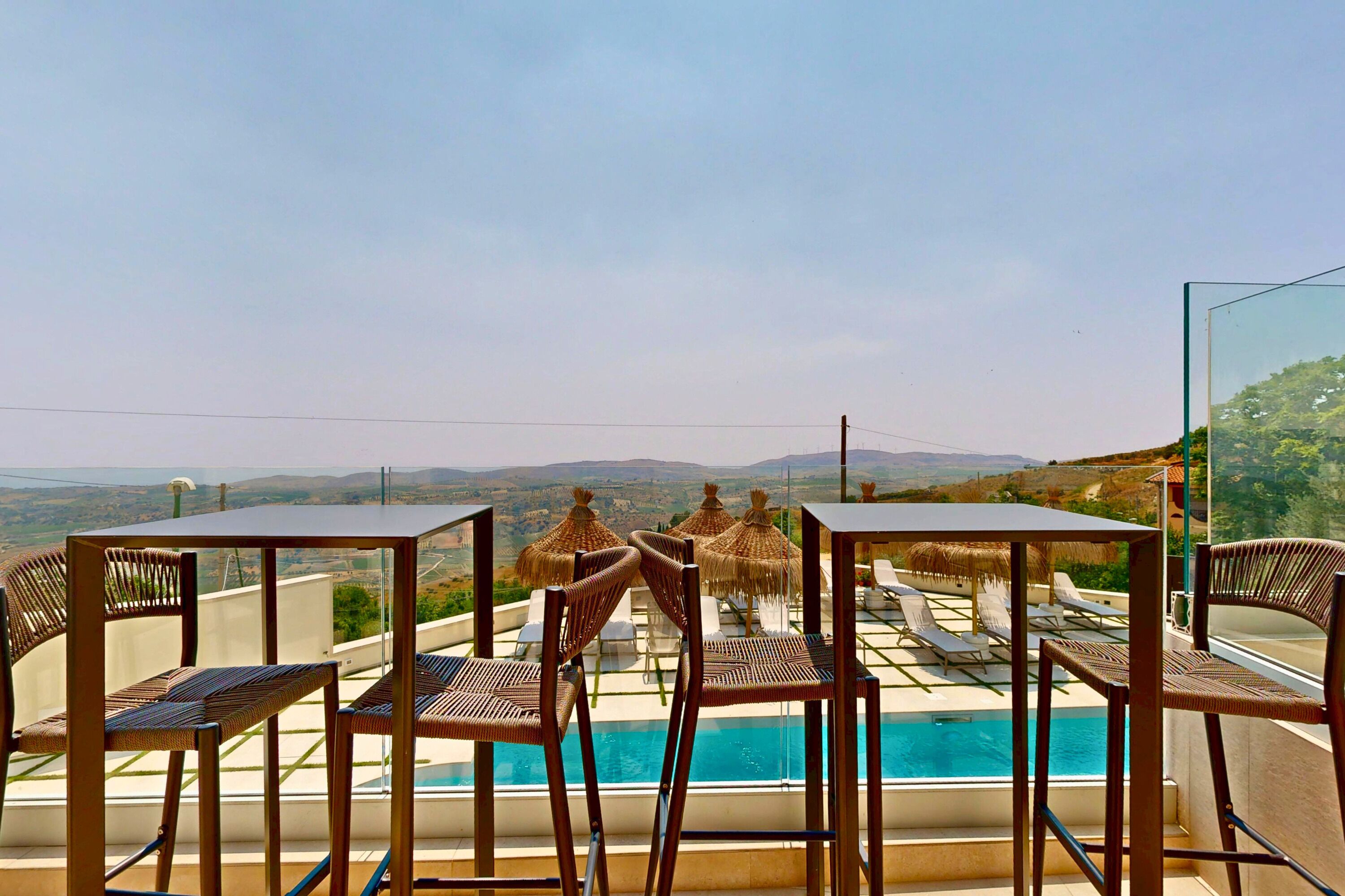 Area piscina con sedie e tavoli, vista panoramica sul paesaggio e una piscina.