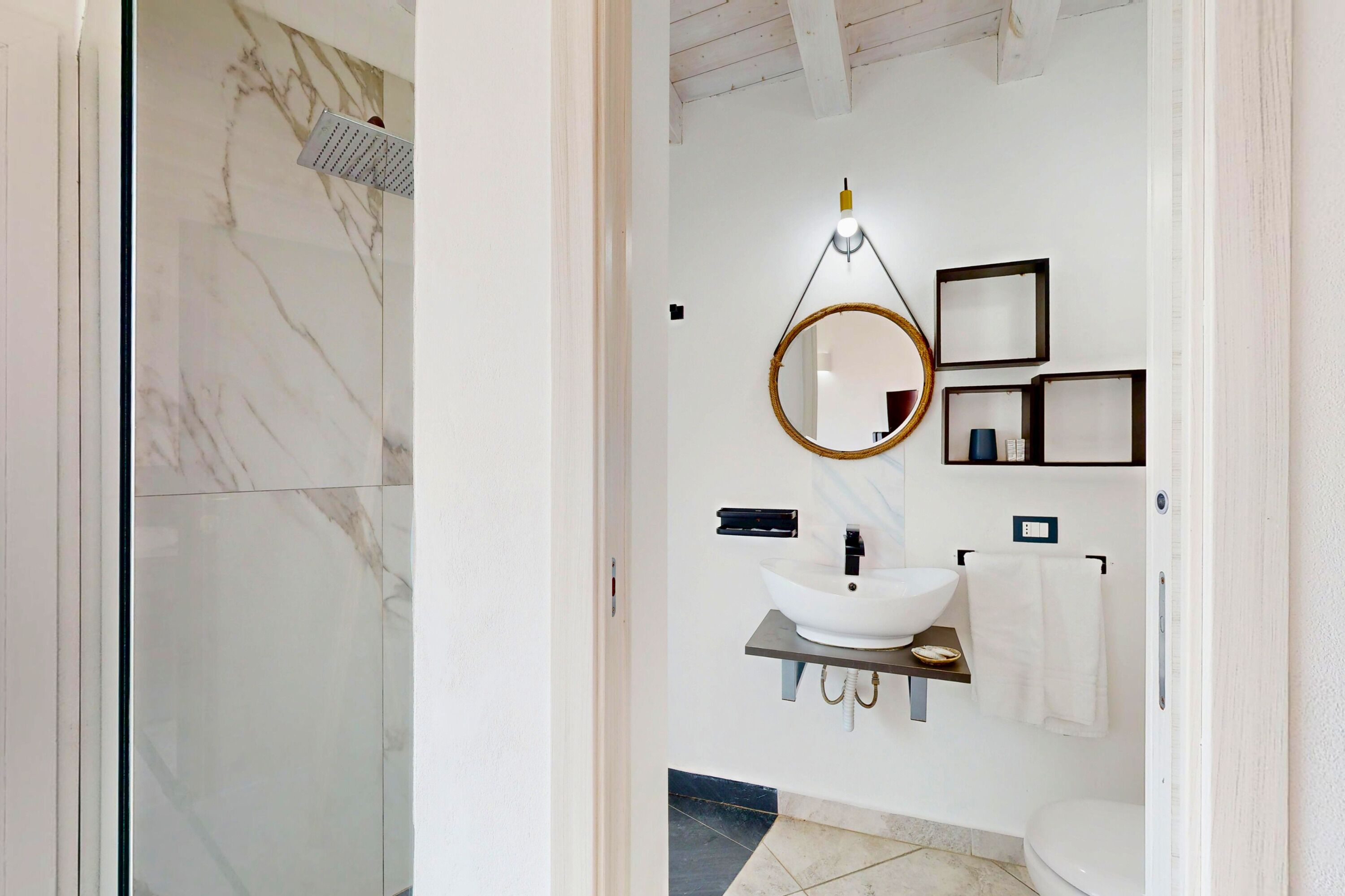 A bathroom with a marble shower, a white sink, and a mirror.