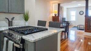 A kitchen with a central island, stainless steel appliances, and a dining area with chairs and a table. - Ironworks Urban Retreat|Pet Friendly|RPI|Hospitals (Troy)