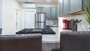 A modern kitchen with grey cabinets, a stainless steel refrigerator, a red coffee maker, and a gas stove. - Ironworks Urban Retreat|Pet Friendly|RPI|Hospitals (Troy)