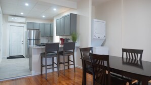A modern kitchen with grey cabinets, stainless steel appliances, and a dining area with wooden chairs and a table. - Ironworks Urban Retreat|Pet Friendly|RPI|Hospitals (Troy)