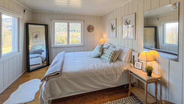 A bedroom with a large bed, a bedside table with a lamp, a mirror, and a window with a view of trees. - Beautiful home in Vestre Gausdal (Vestre Gausdal)