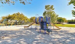 Explore the playground area with a slide, climbing frame, and swing set set amidst trees and open space.