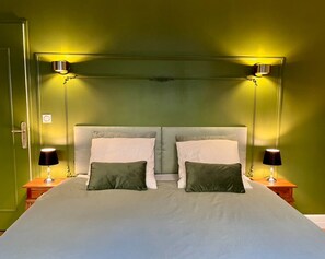 A bed with a grey headboard, two bedside lamps, and a green wall.