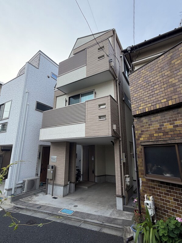 A multi-story residential building with a flat roof, a balcony, and a ground-level entrance.