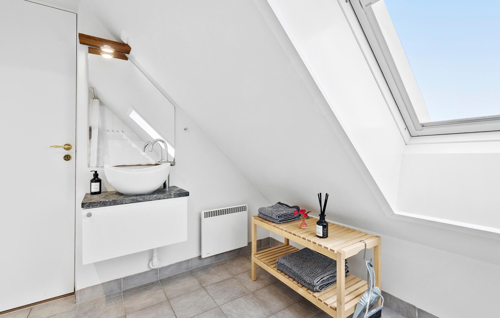 A modern bathroom with a skylight, a white sink, and a wooden shelf with towels and toiletries.