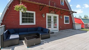Een rode houten woning met een overdekt terras, een blauwe bank en een bloemenmand.