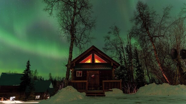 A cabin with a wooden exterior, a front porch, and a snow-covered ground. - The Loon's Nest Cabin (Trapper Creek)