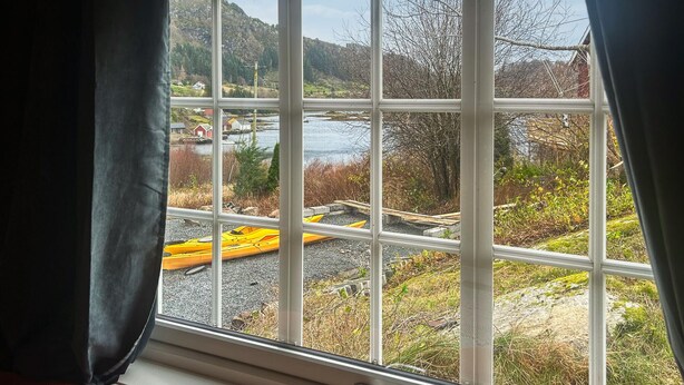 Una ventana con vistas a un río, barcos y un paisaje montañoso.