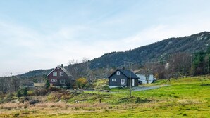 Paisaje rural con dos casas, una roja y otra azul oscura, rodeadas de campos verdes y colinas.