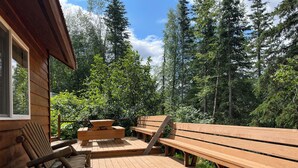A wooden deck with picnic tables and benches, surrounded by dense forest. - Beaver's Hideaway Cabin (Trapper Creek)