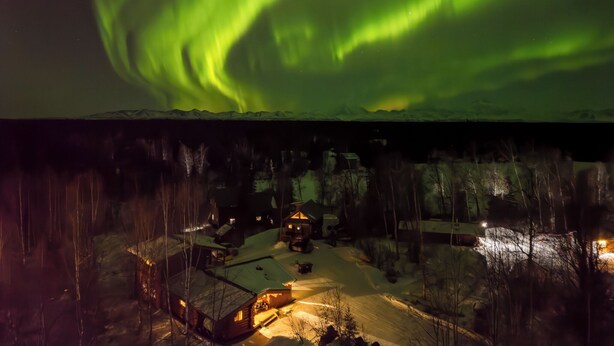 A snowy landscape with houses and a visible aurora borealis. - Beaver's Hideaway Cabin (Trapper Creek)