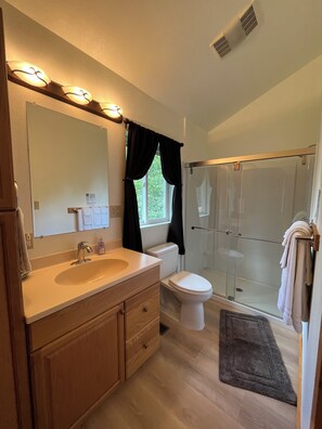 A bathroom with a sink, mirror, toilet, and shower. - Beaver's Hideaway Cabin (Trapper Creek)