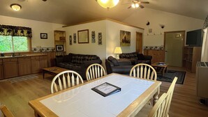 A spacious living area with a dining table, multiple chairs, a kitchen in the background, and ceiling fans. - Beaver's Hideaway Cabin (Trapper Creek)