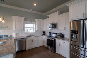 A modern kitchen with white cabinetry, stainless steel appliances, and a granite countertop. - Yellow Rose of Texas (Crystal Beach)