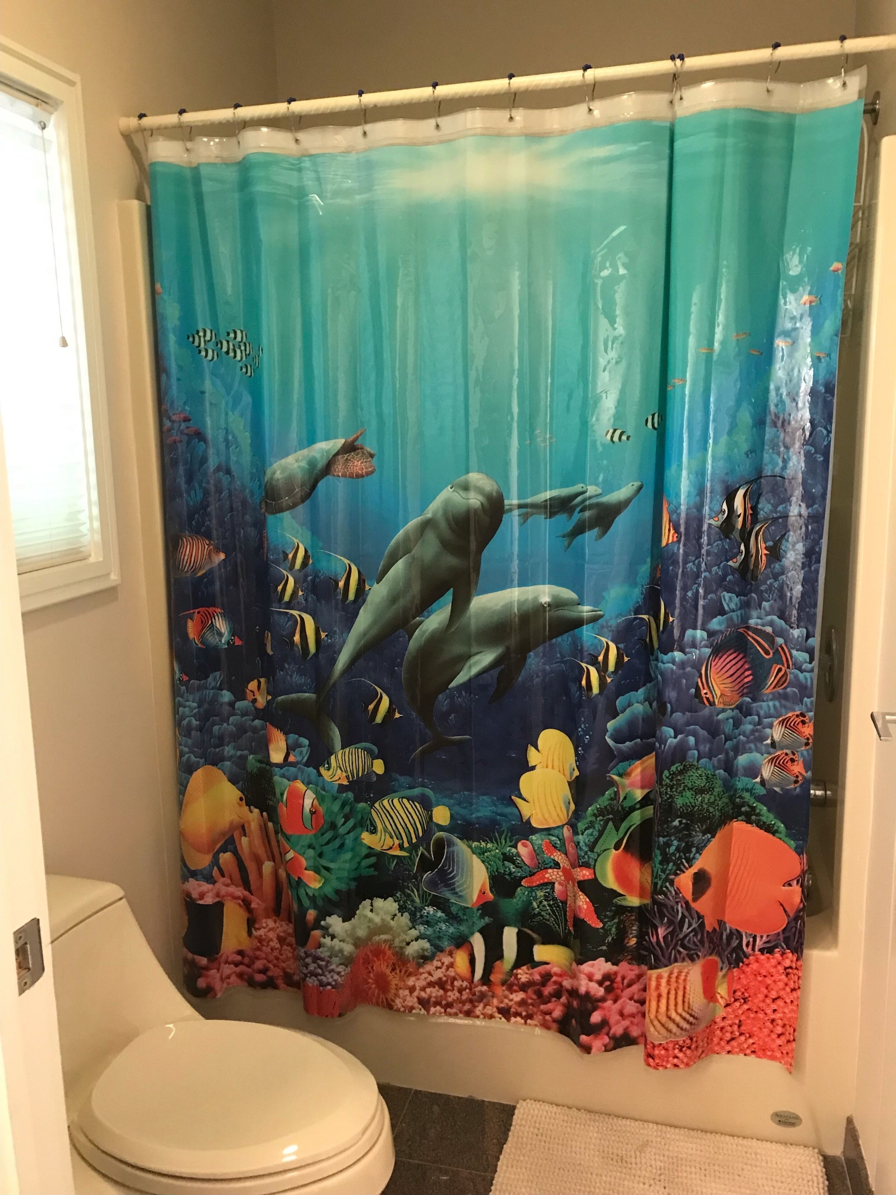 A bathroom with a shower curtain depicting an underwater scene, a toilet, and a rug on the floor.