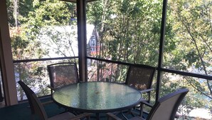 A round glass table with four chairs, surrounded by a glass railing, overlooking a view of trees and a building.