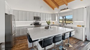Cocina moderna con armarios blancos, una isla grande con taburetes de bar, un refrigerador de acero inoxidable y techo de madera.