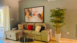 Un salon avec un canapé beige, une table basse, un grand tableau abstrait et un plant de bambou en pot.