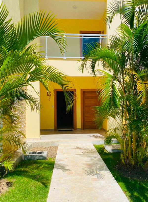 A two-story building with a yellow facade, a covered entrance, and a pathway leading to the entrance.