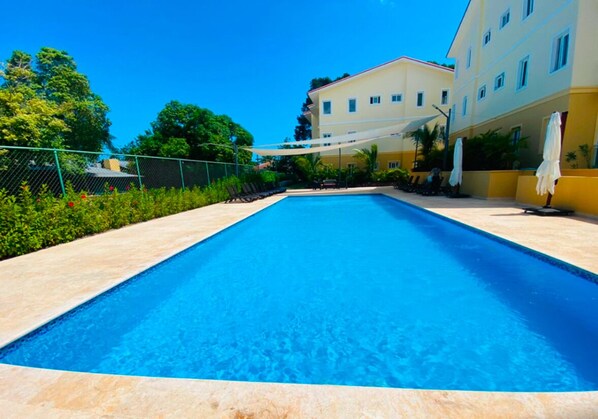 Ein rechteckiger Pool mit glasklar blauem Wasser, umgeben von einem hell gefliesten Deck.